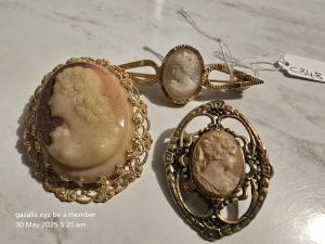 Vintage Cameo Brooch Trio Three vintage cameo brooches with carved profiles in ornate gold-tone frames on a light surface.