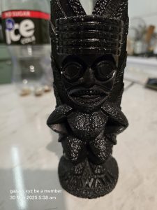 Black tiki statue with "Hawaii" inscribed, bottle labeled "ice cola" in background.