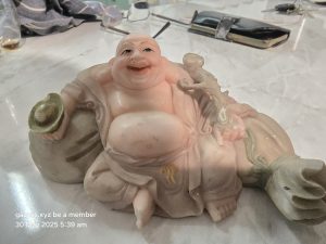 Marble figurine of joyful figure with large belly, holding object, on reflective surface.