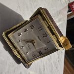 Vintage Gold-Toned Alarm Clock Display Vintage gold alarm clock with price tag on light surface, time and website text visible.