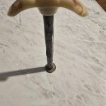 Metal Pole with Teeth-Like Top Metal pole with tan, tooth-like top on a textured surface, text with date visible in corner.