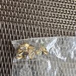 Gold Jewelry Components in Plastic Bag Close-up of a plastic bag with gold-colored metal components on a woven surface.
