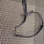 Braided Bracelet with Cross Pendant Black braided bracelet with cross pendant on a woven textured surface.