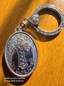 Silver keychain with ornate cross pendant and heart accent on wooden surface in sunlight.