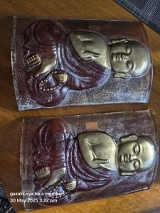 Two metallic relief plaques showing figures in meditative poses with prayer beads on wood.