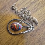 Colorful Abstract Pendant on Gold Chain Gold chain necklace with oval pendant of colorful swirls on a wooden surface.