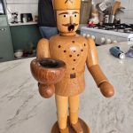 Miner Figurine in Kitchen Setting Wooden miner figurine in foreground, bowl in hand, kitchen setting with counter items visible.