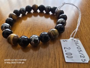Beaded bracelet with tiger's eye beads on wood surface, price tag $2.00, date 26/05/25.