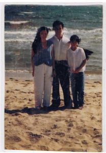 Family Enjoying a Sunny Beach Day Three people on a sunny beach with waves, wearing casual summer clothes.