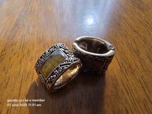 Ornate metal rings with inlaid stones on wood surface; timestamp bottom left corner.