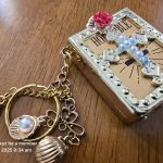 Golden Religious Keychain with Ornate Charms Decorative golden keychain with book charm, pearl cross, and various smaller charms on wood surface.