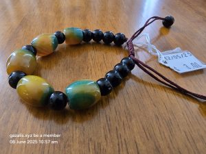 Beaded bracelet with multicolored and black beads, dark red cord, $3.00 tag on wood surface.