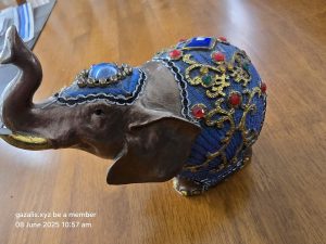 Decorative elephant figurine on wood, adorned with blue fabric, gold patterns, and jewels.