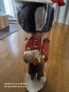 Toy Soldier in Display Case Toy soldier in red uniform with drum in clear cylindrical case on wooden table.
